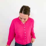 Person wearing a bright pink cardigan and blue jeans against a white background