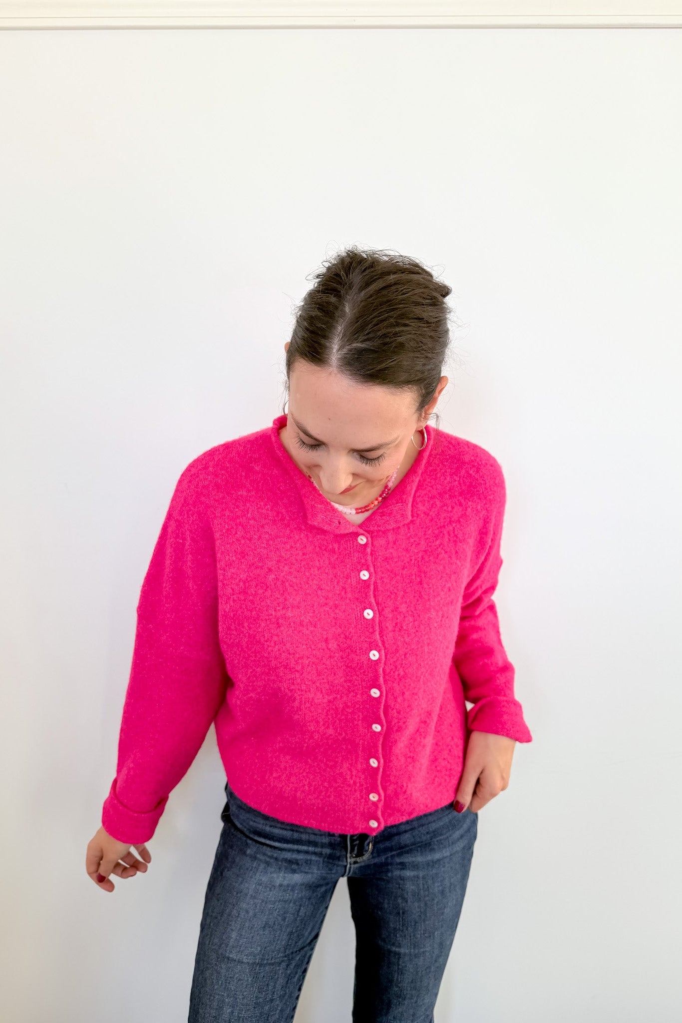 Person wearing a bright pink cardigan and blue jeans against a white background