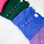 Folded shirts in pink, green, blue, and purple on a white surface