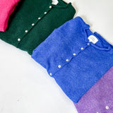 Folded shirts in pink, green, blue, and purple on a white surface