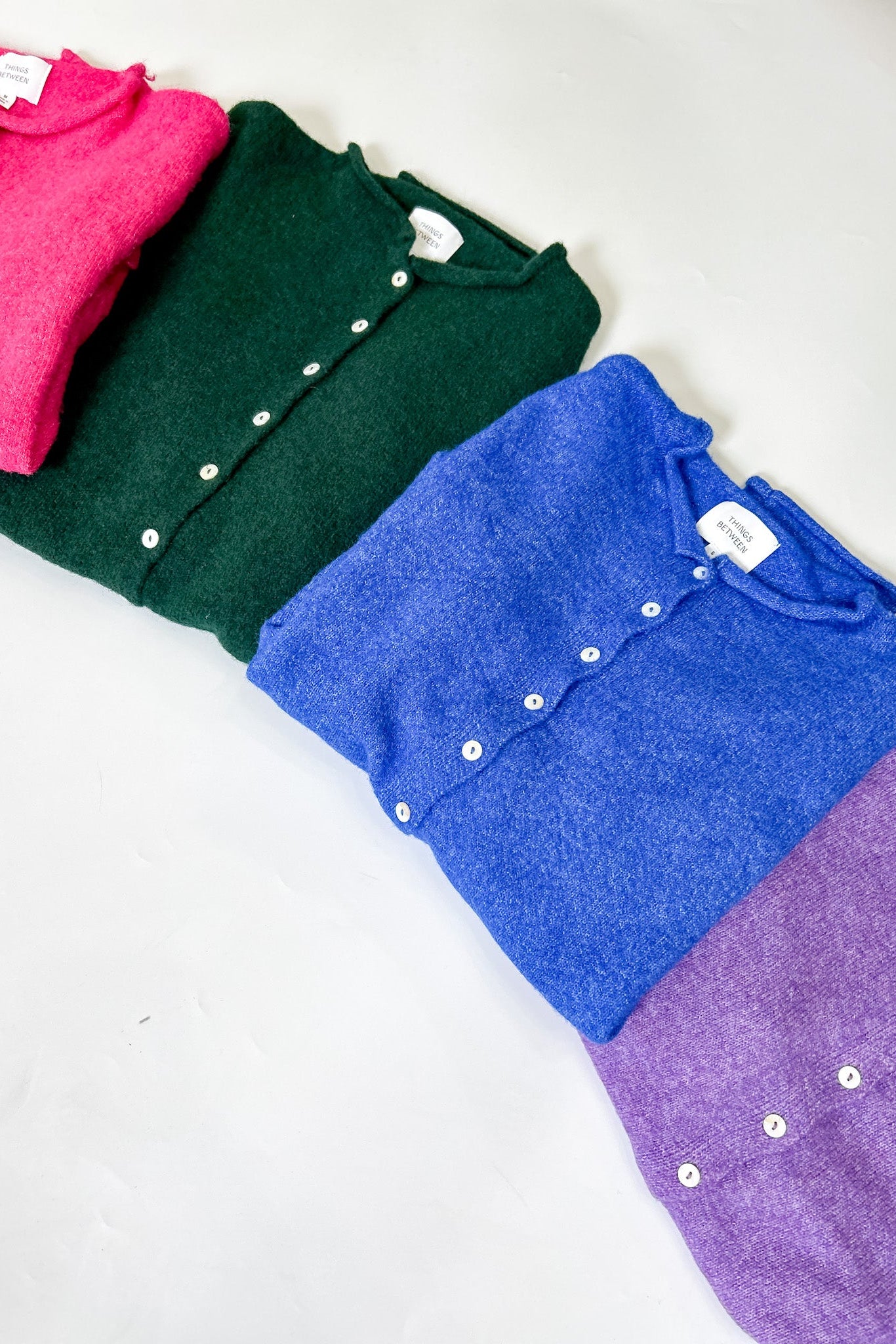 Folded shirts in pink, green, blue, and purple on a white surface
