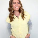 Woman wearing a light yellow vest over a gray shirt with a white background