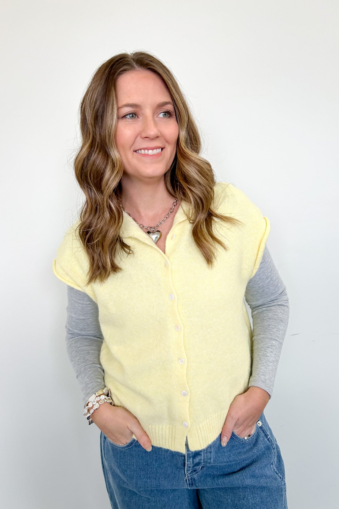 Woman wearing a light yellow vest over a gray shirt with a white background