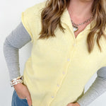 Woman wearing a light yellow cardigan over a gray shirt with blue jeans against a white background