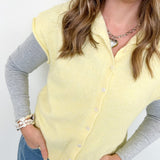 Woman wearing a light yellow cardigan over a gray shirt with blue jeans against a white background