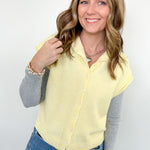 Woman wearing a yellow cardigan over a gray long-sleeve shirt with blue jeans against a white background