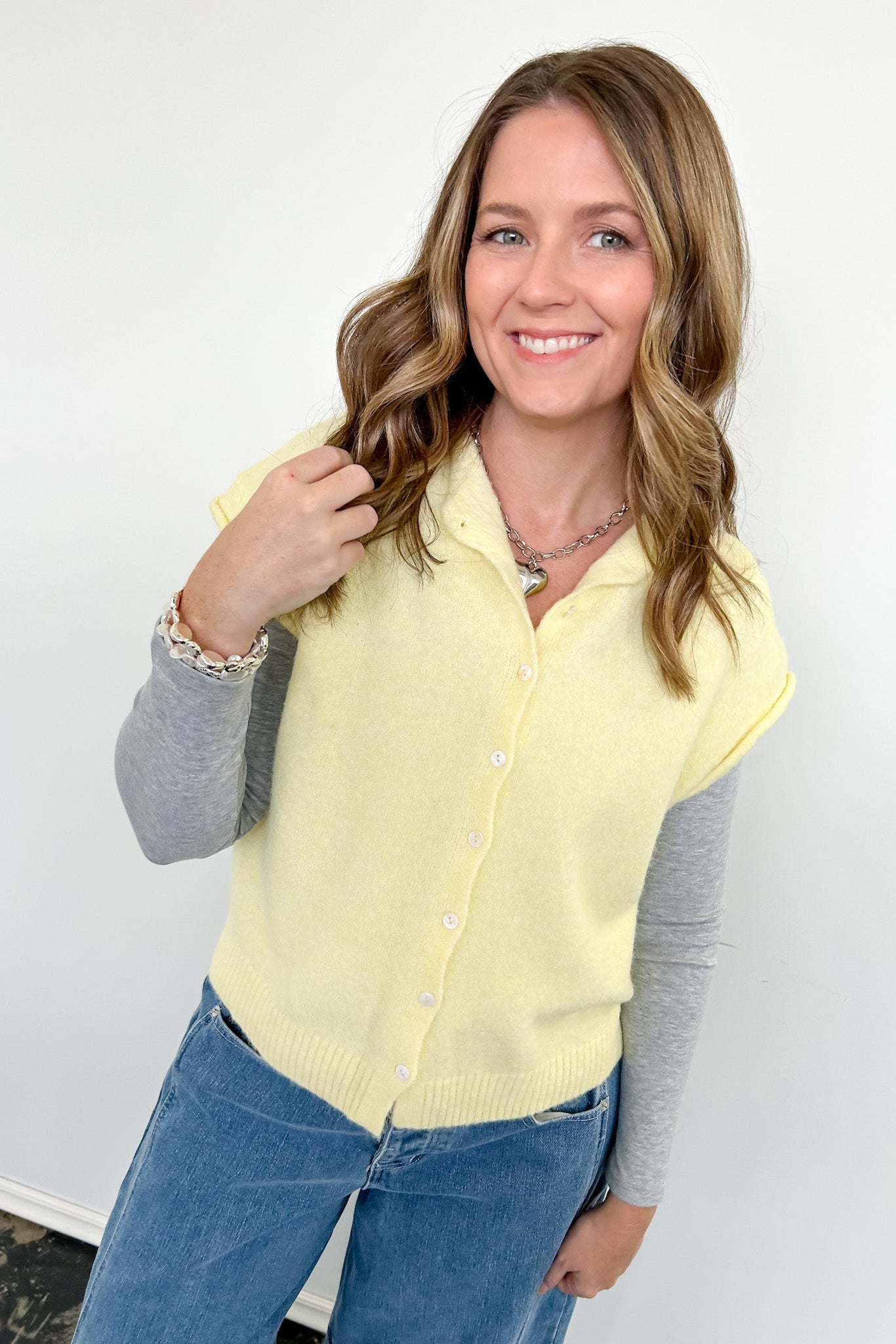Woman wearing a yellow cardigan over a gray long-sleeve shirt with blue jeans against a white background