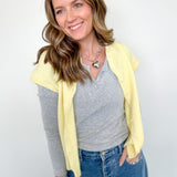 Woman wearing a yellow cardigan, gray shirt, and blue jeans against a white background