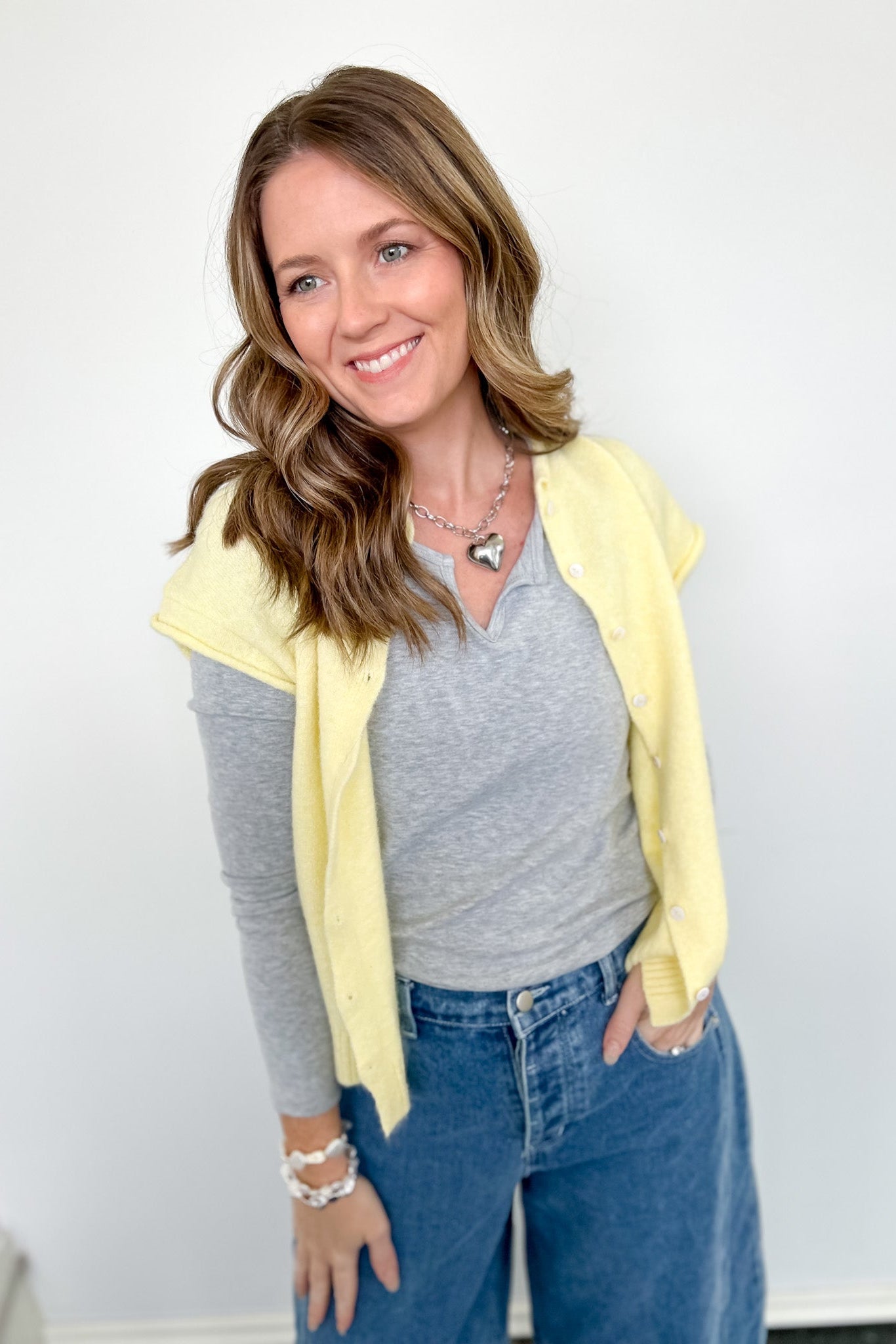 Woman wearing a yellow cardigan, gray shirt, and blue jeans against a white background