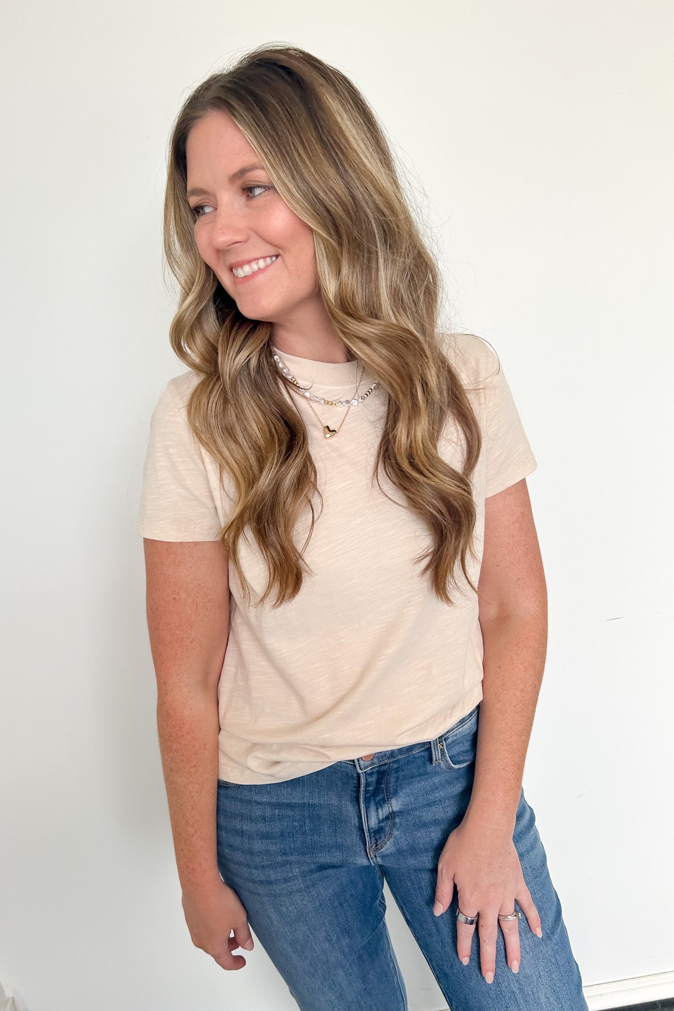 Woman wearing a beige t-shirt and blue jeans against a white background
