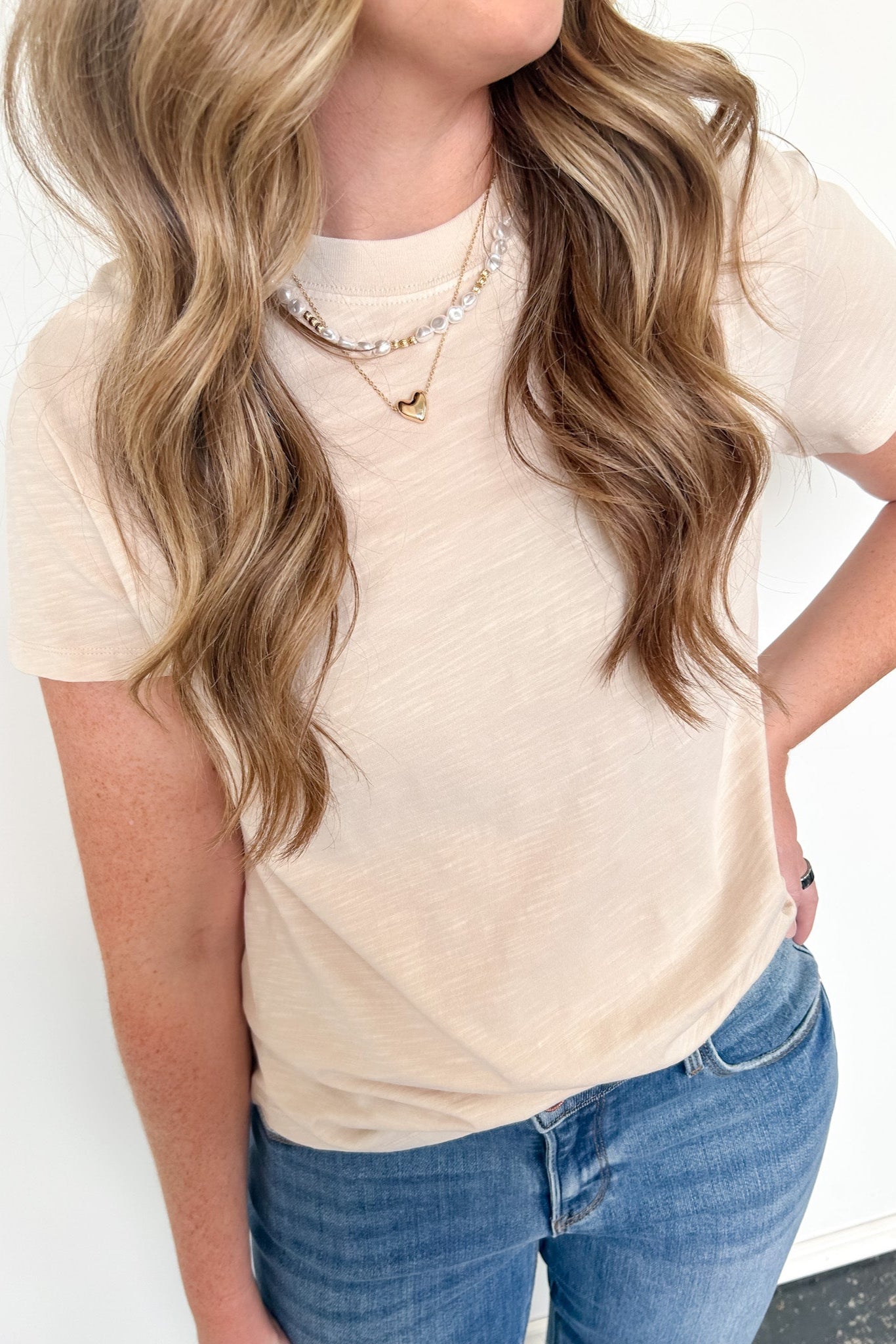 Person wearing a beige top and blue jeans with a plain background