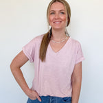 Woman wearing a light pink v neck tee against a white wall