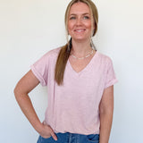 Woman wearing a light pink v neck tee against a white wall