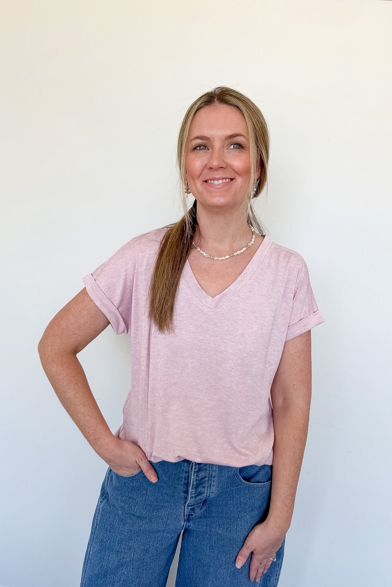 Woman wearing a light pink v neck tee against a white wall