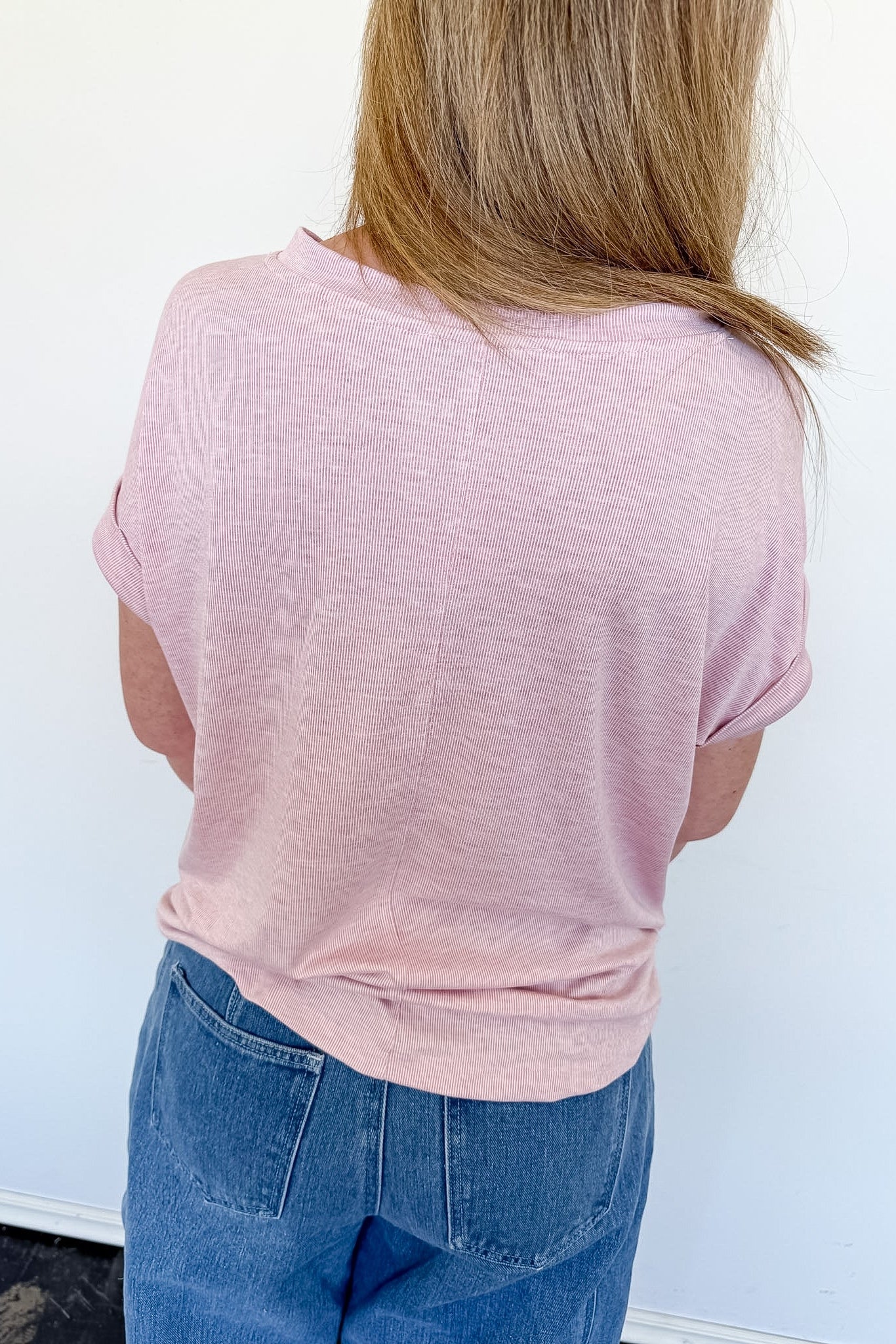 Person wearing a pink shirt and blue jeans against a white background
