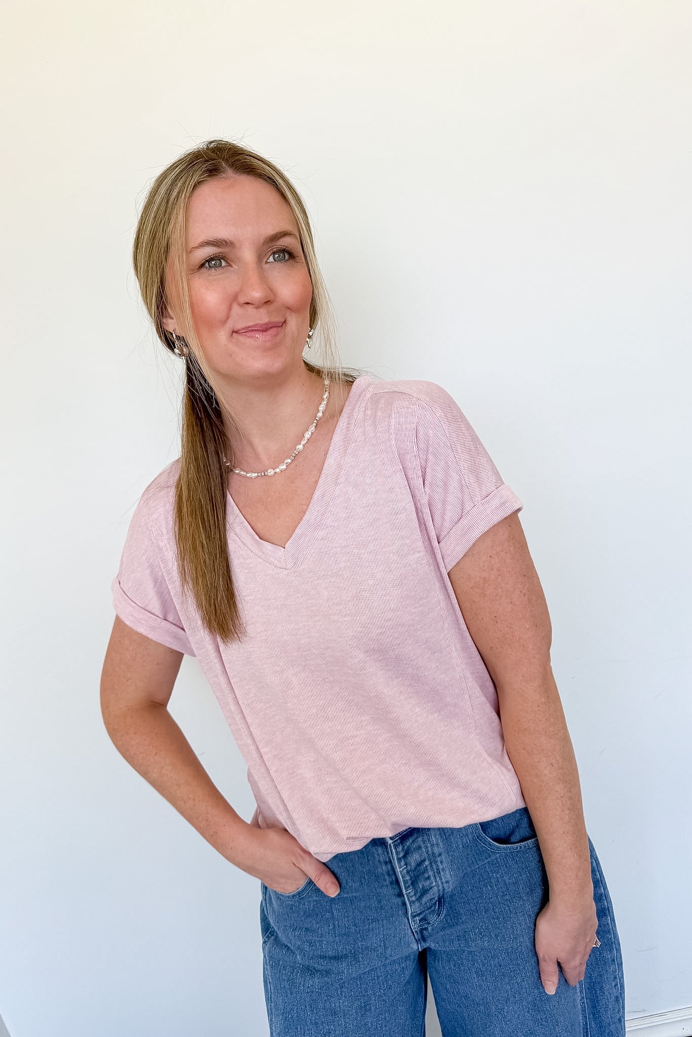 Woman standing with her hand in her pocket in a light pink v neckline tee
