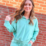 Woman in a teal tracksuit standing against a brick wall