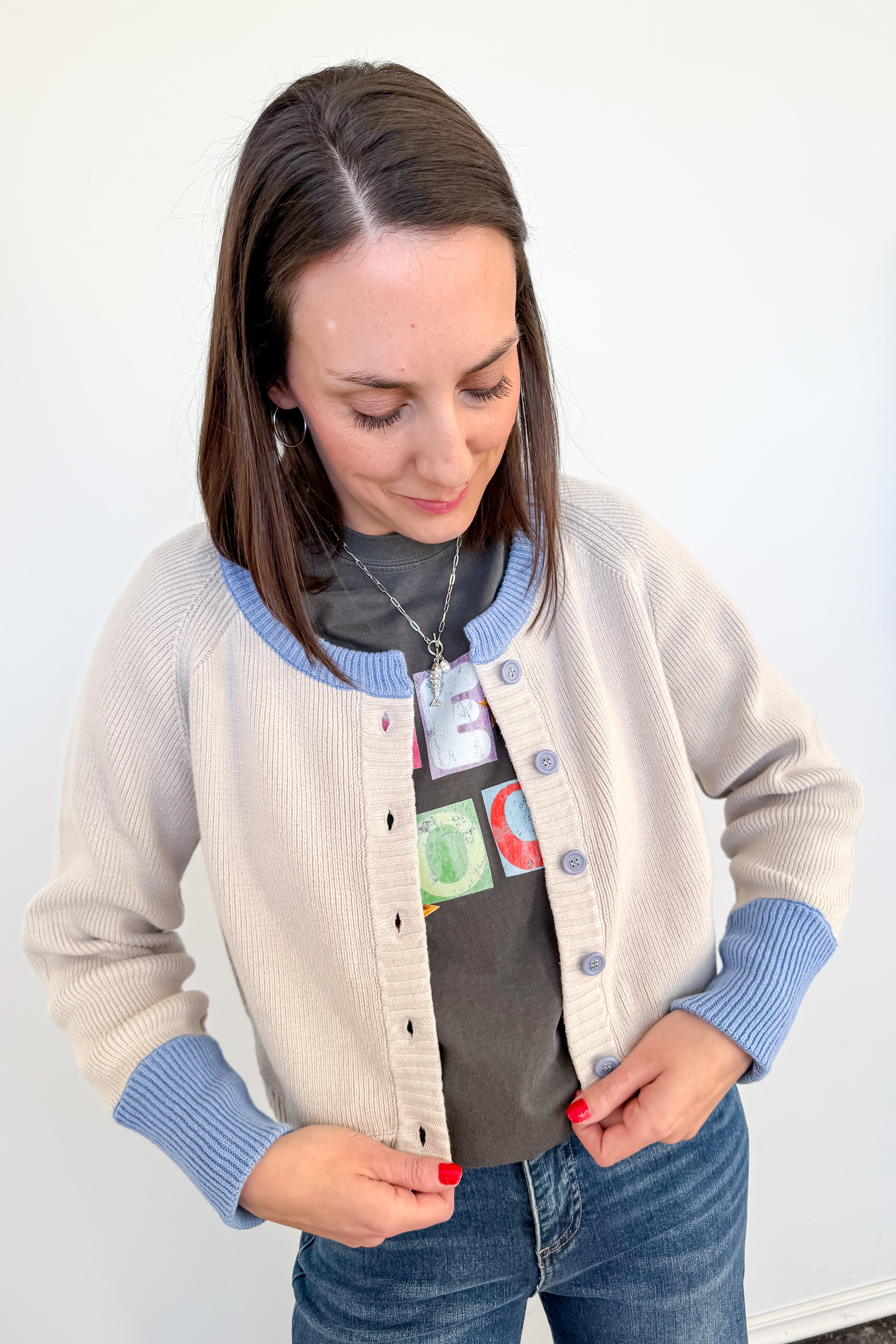 Woman wearing a beige cardigan with blue sleeves and a gray shirt with colorful designs.