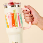 Hand holding a tumbler with colorful designs on a beige background