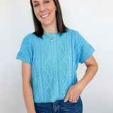 Woman wearing a blue knitted shirt and jeans against a white background