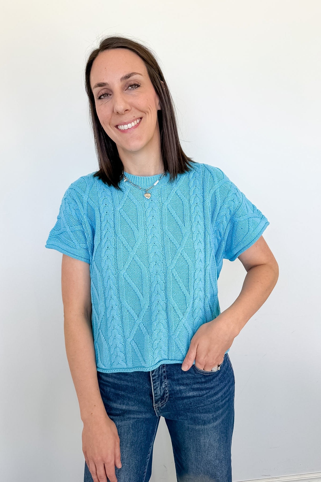 Woman wearing a blue knitted shirt and jeans against a white background
