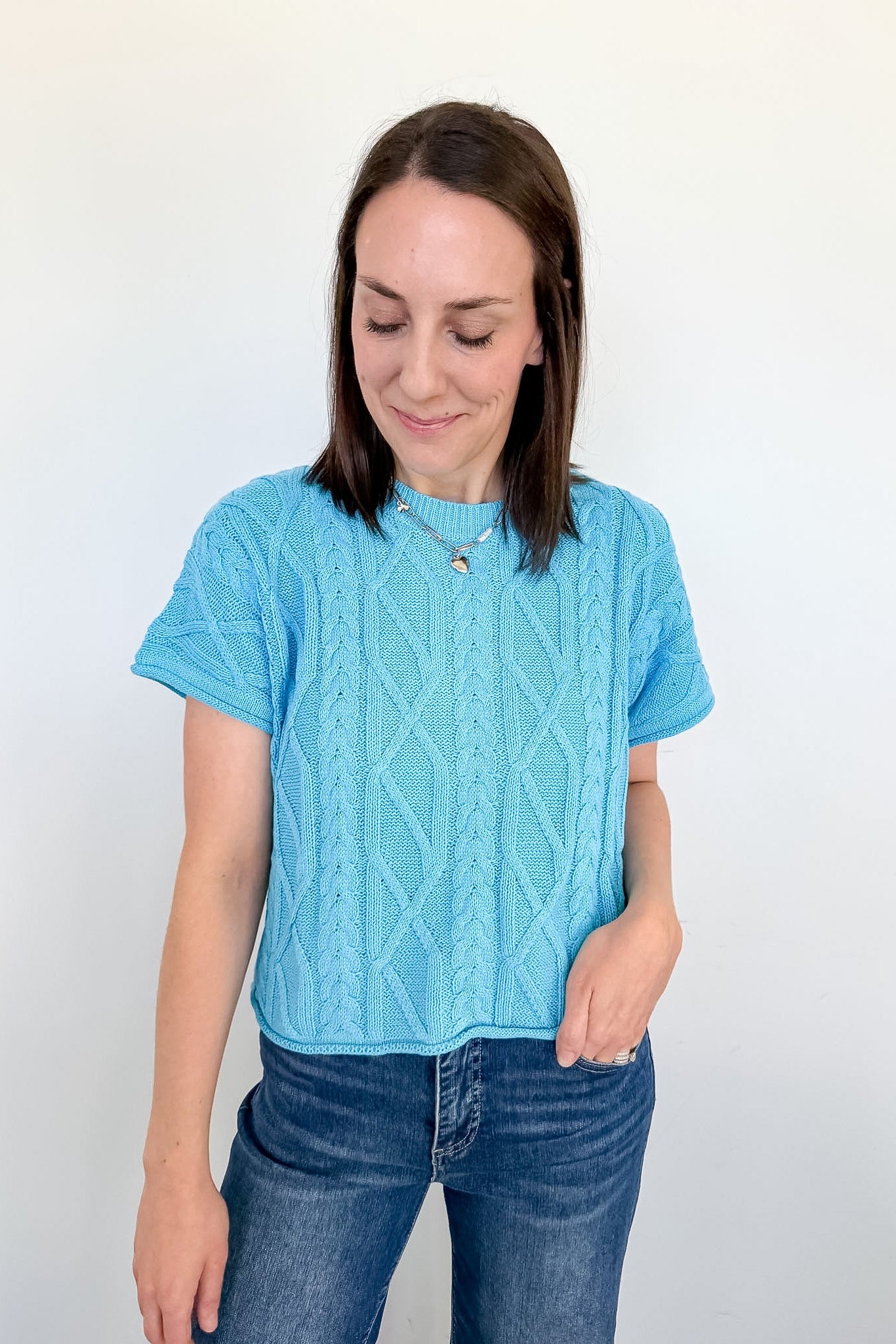 Woman wearing a blue knitted sweater and jeans against a white background