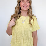Woman wearing a yellow cable knit top and blue jeans against a white background