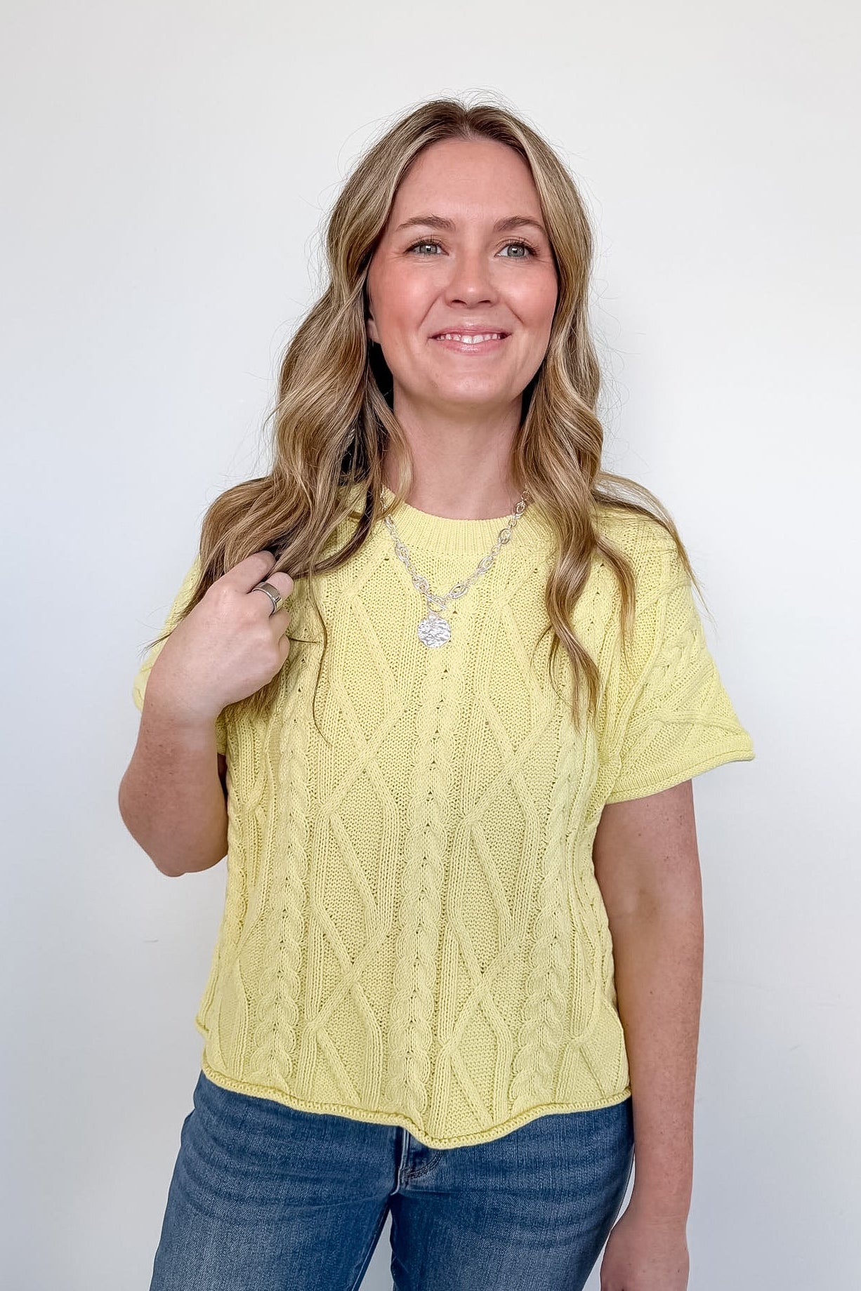 Woman wearing a yellow cable knit top and blue jeans against a white background