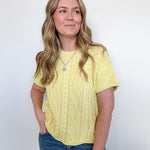 Woman wearing a yellow cable knit top and blue jeans against a white background