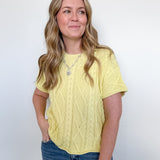 Woman wearing a yellow cable knit top and blue jeans against a white background