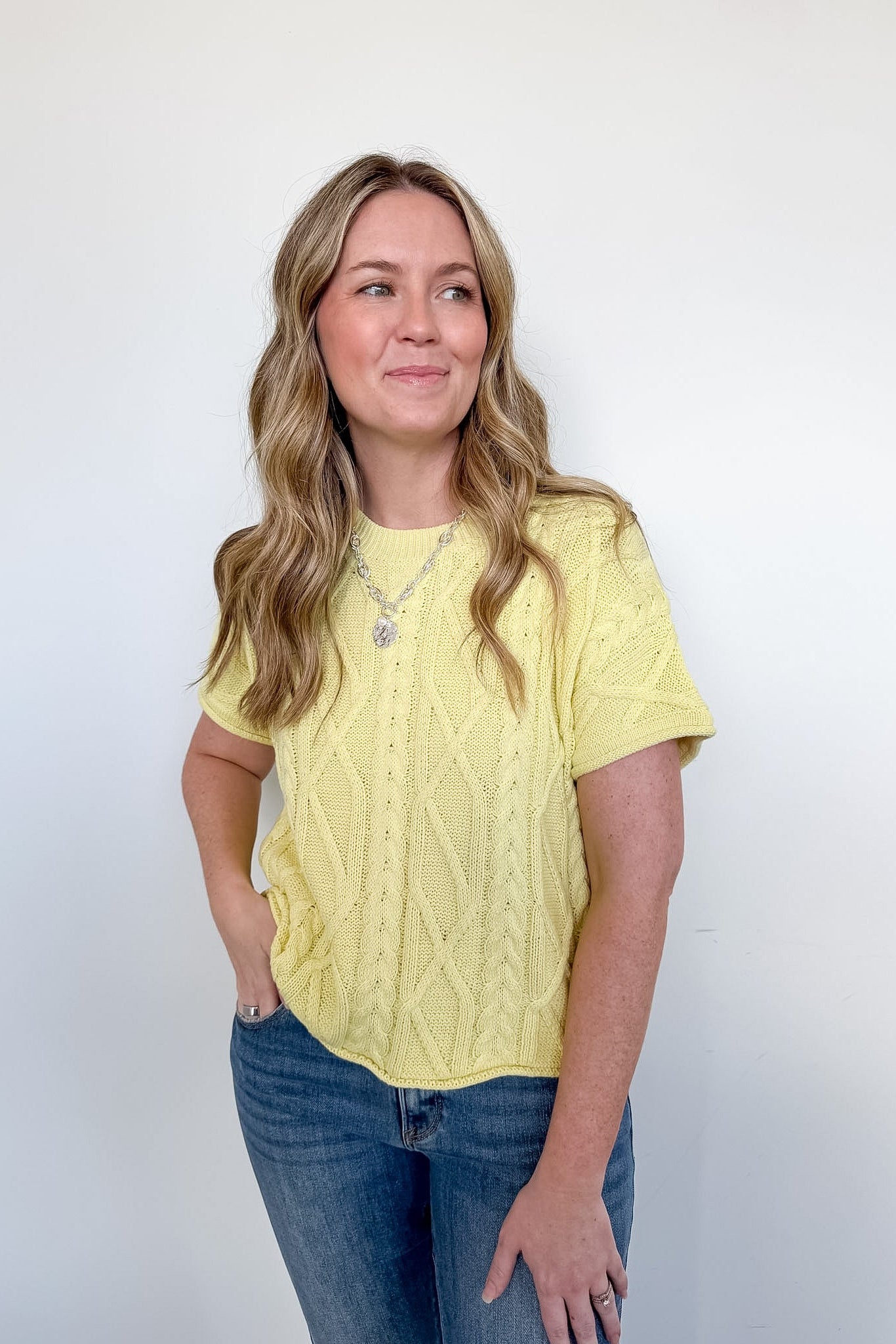 Woman wearing a yellow cable knit top and blue jeans against a white background
