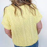 Person wearing a yellow cable knit sweater and blue jeans against a white background