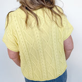 Person wearing a yellow cable knit sweater and blue jeans against a white background