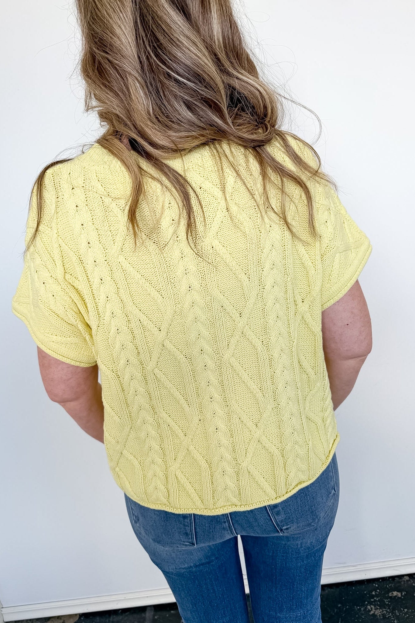 Person wearing a yellow cable knit sweater and blue jeans against a white background