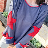 Person wearing a blue sweatshirt with red star designs outdoors.