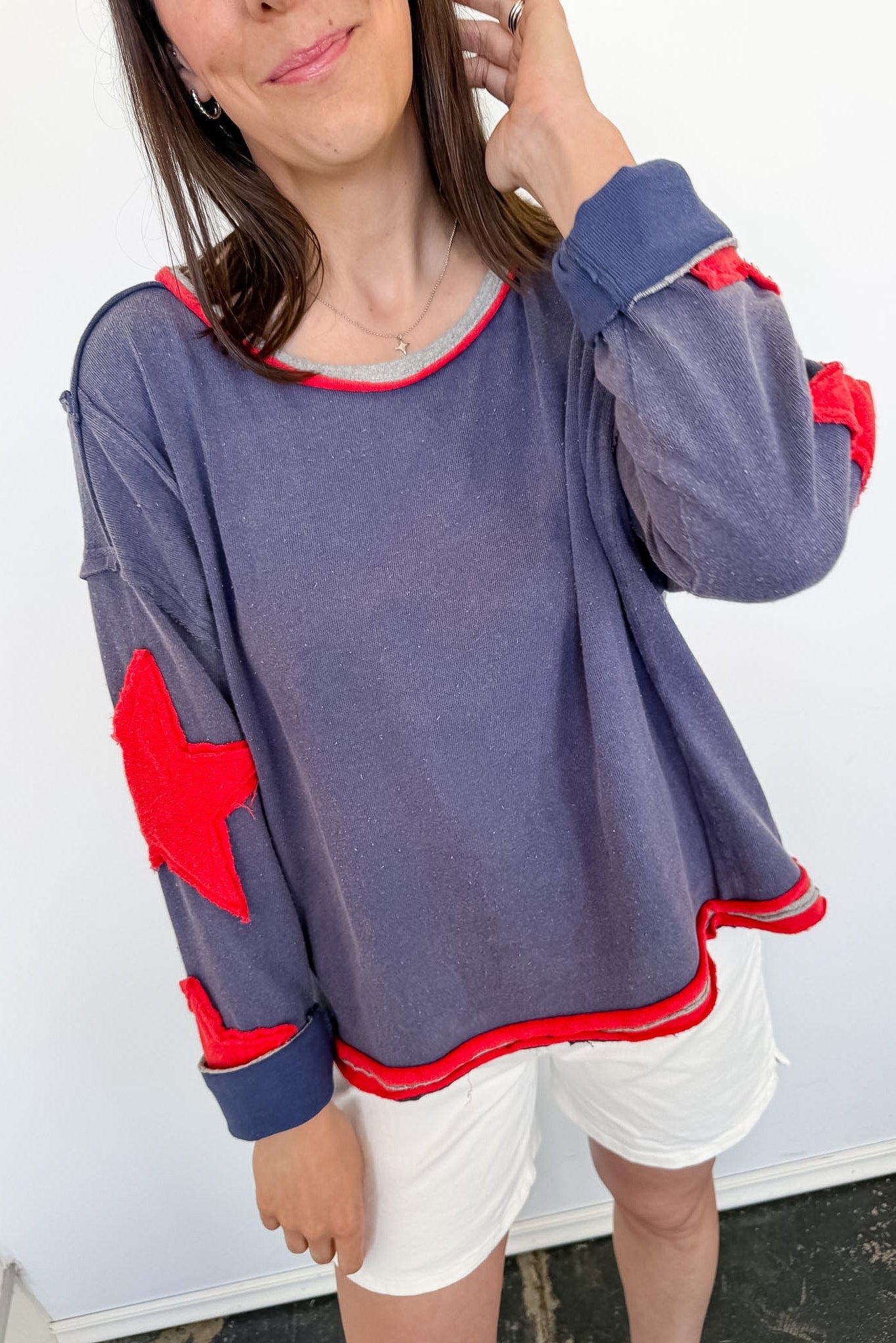Person wearing a gray sweatshirt with red elbow patches and white shorts against a white background