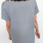 Person wearing a black and white checkered dress against a white wall.