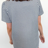 Person wearing a black and white checkered dress against a white wall.