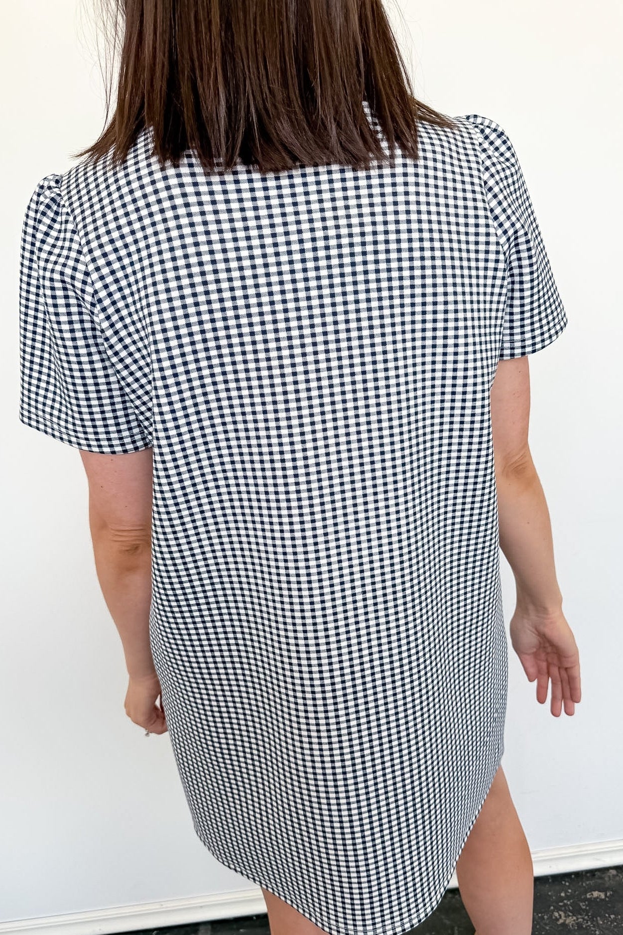 Person wearing a black and white checkered dress against a white wall.