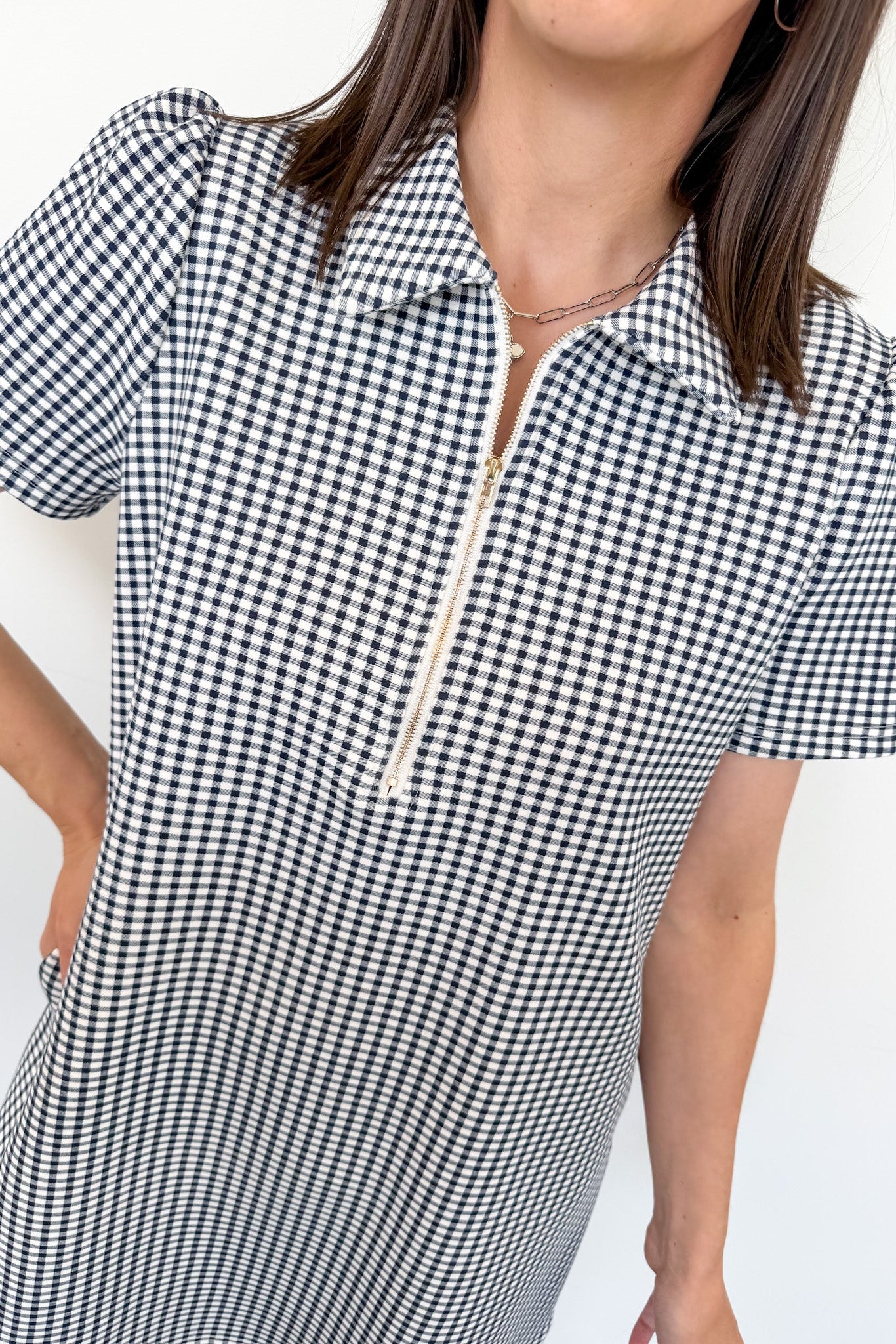 Person wearing a black and white checkered dress with a zipper detail on a white background