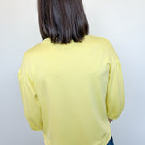 Person wearing a yellow long-sleeve top and blue jeans against a white wall.