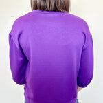 Person wearing a purple sweater from behind with a plain background