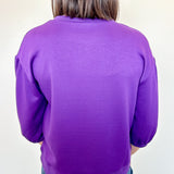 Person wearing a purple sweater from behind with a plain background
