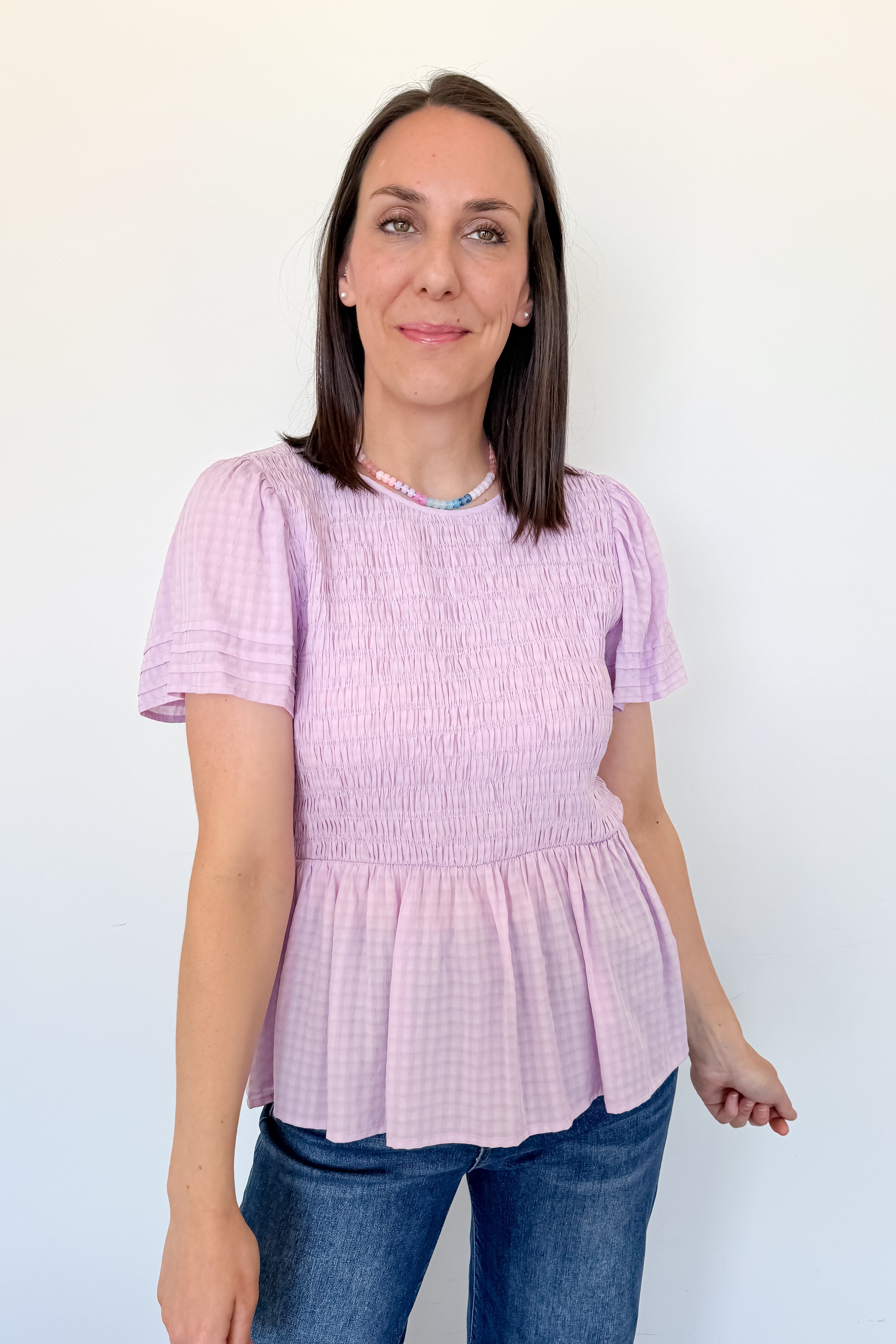 Woman wearing a pink smocked top and blue jeans against a white wall