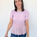 Woman wearing a pink smocked top and blue jeans against a white background