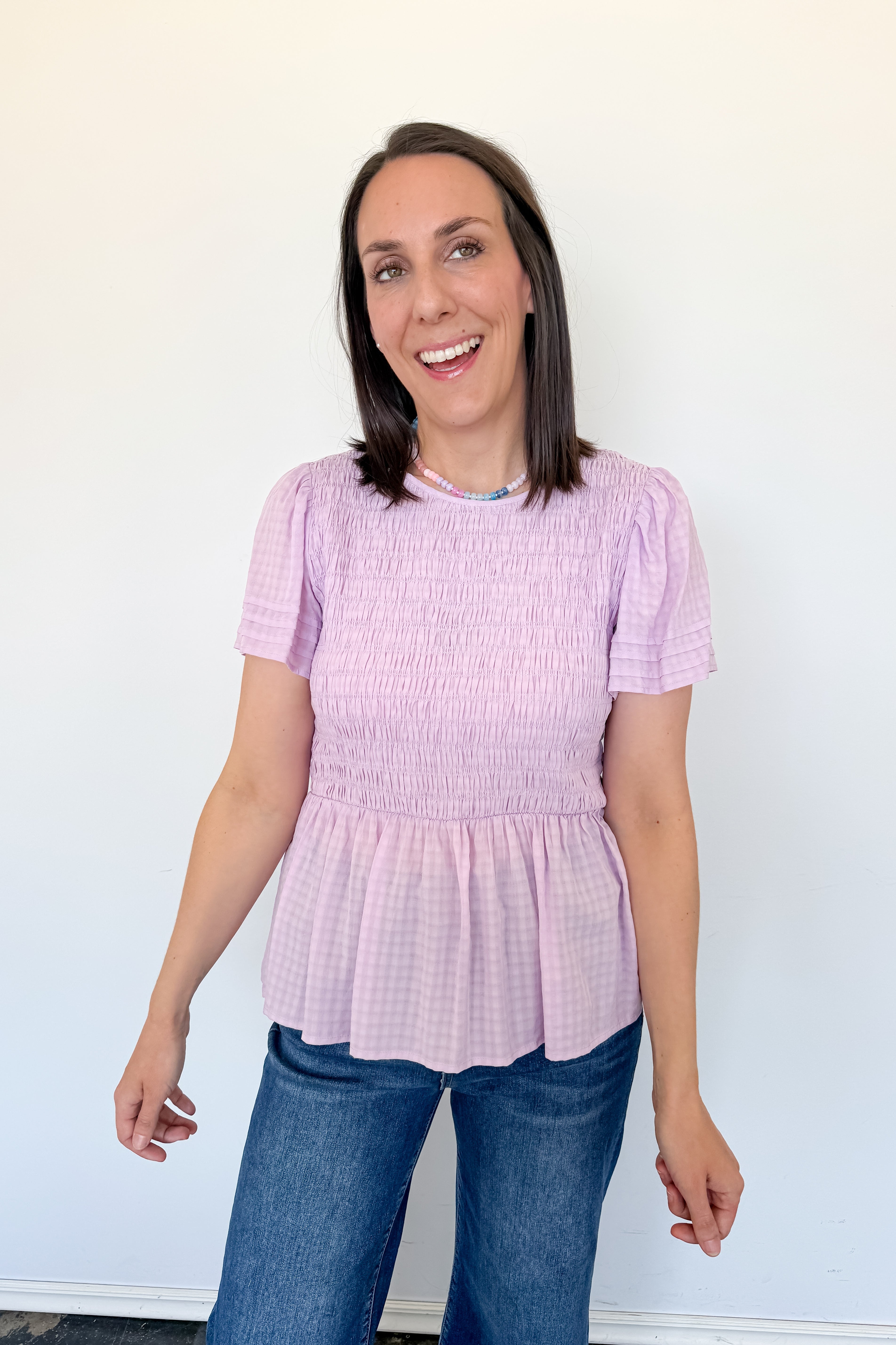 Woman wearing a pink smocked top and blue jeans against a white background