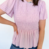 Person wearing a light purple smocked top and blue jeans against a white background