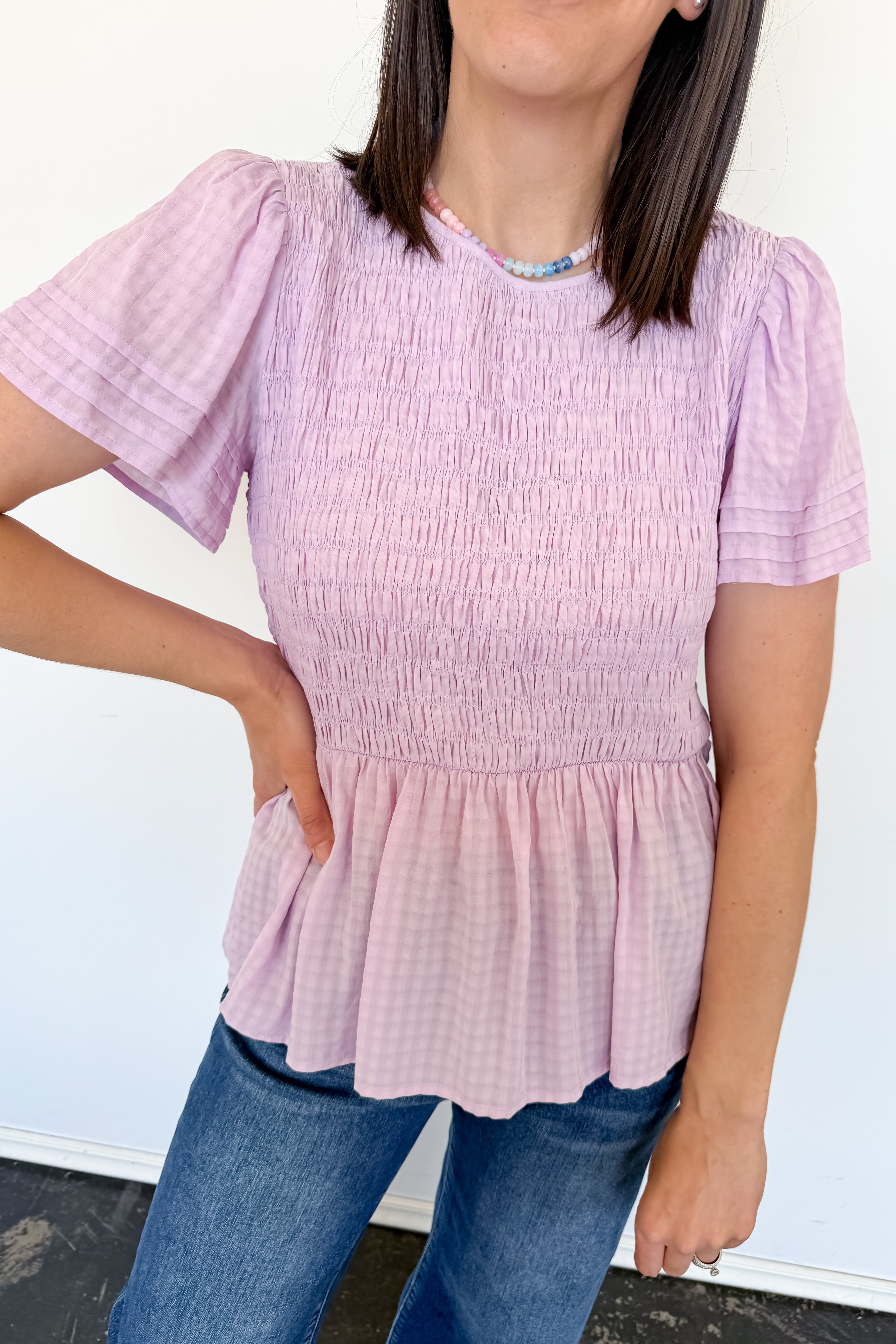Person wearing a light purple smocked top and blue jeans against a white background