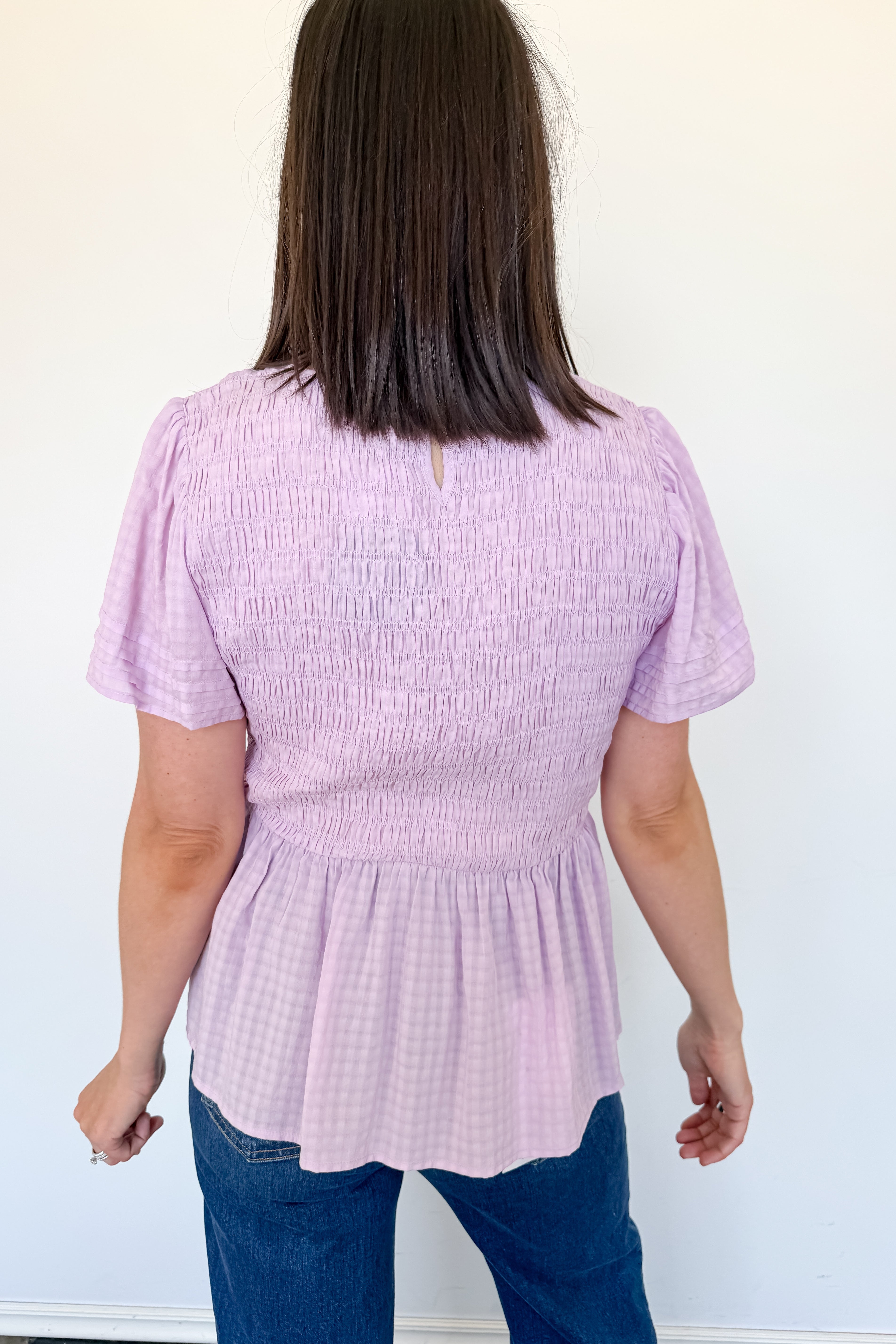 Woman wearing a light purple textured top and blue jeans against a white background