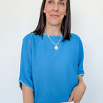 Woman wearing a blue top and white pants against a plain background